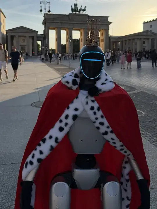 Humanoider Roboter als König Ludwig II. mit Krone und Hermelinumhang vor dem Brandenburger Tor