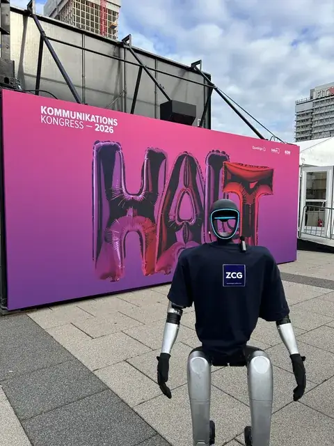 Humanoider Roboter im Shirt mit ZCG-Logo vor der Wand des Kommunikationskongresses